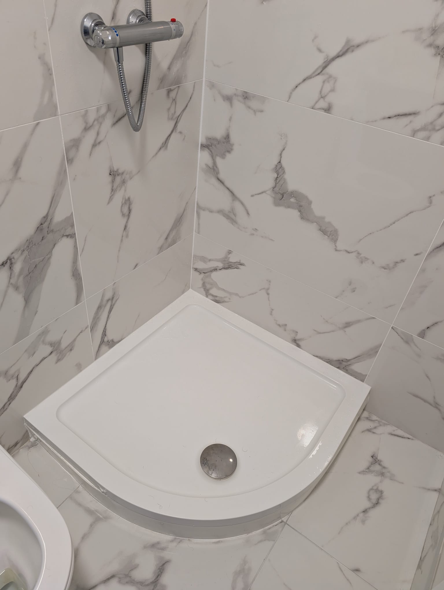 Corner shower tray installation with marble-effect wall tiling in Dublin bathroom