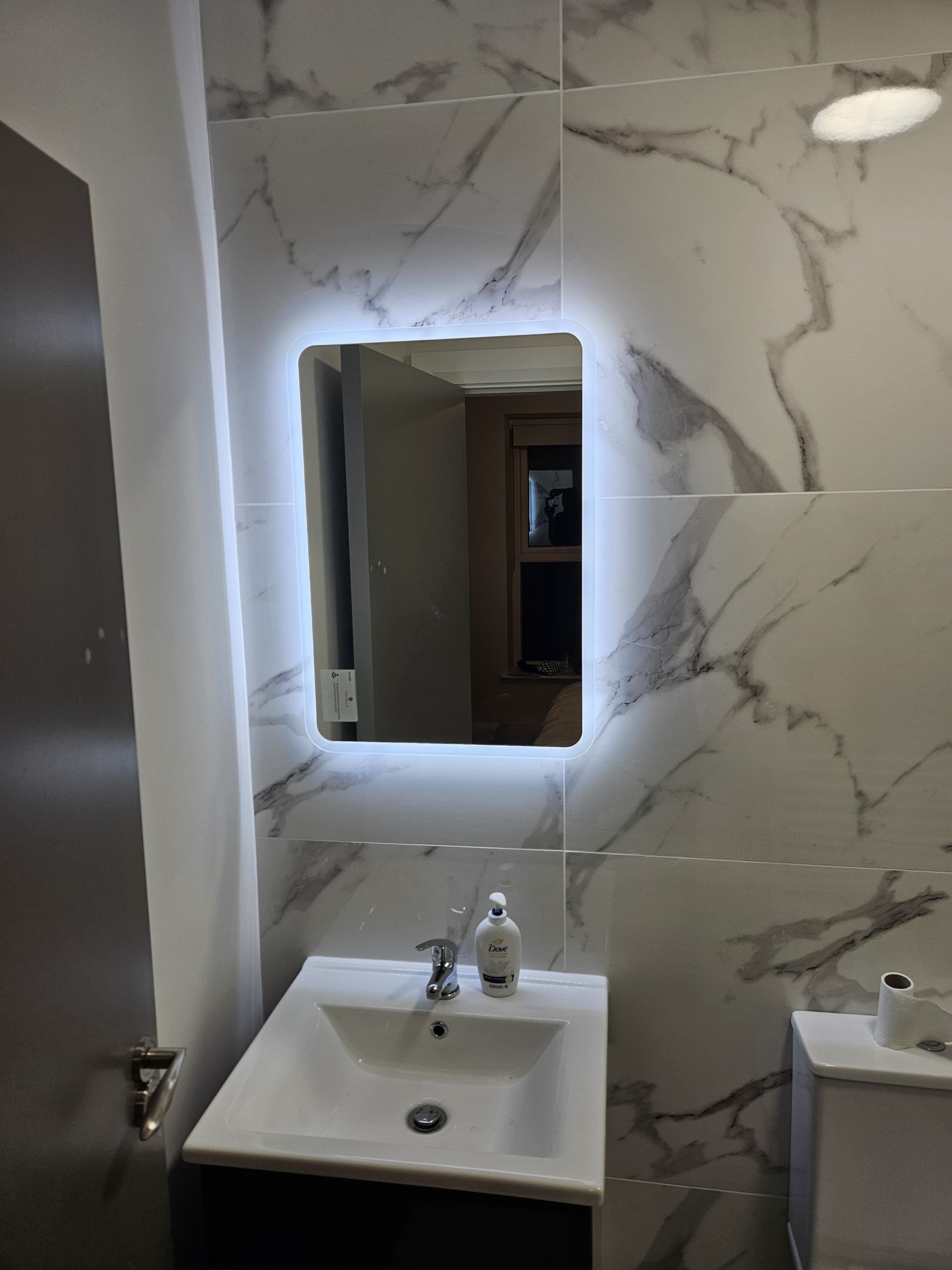 Backlit LED mirror and vanity unit installed in marble-tiled Dublin bathroom