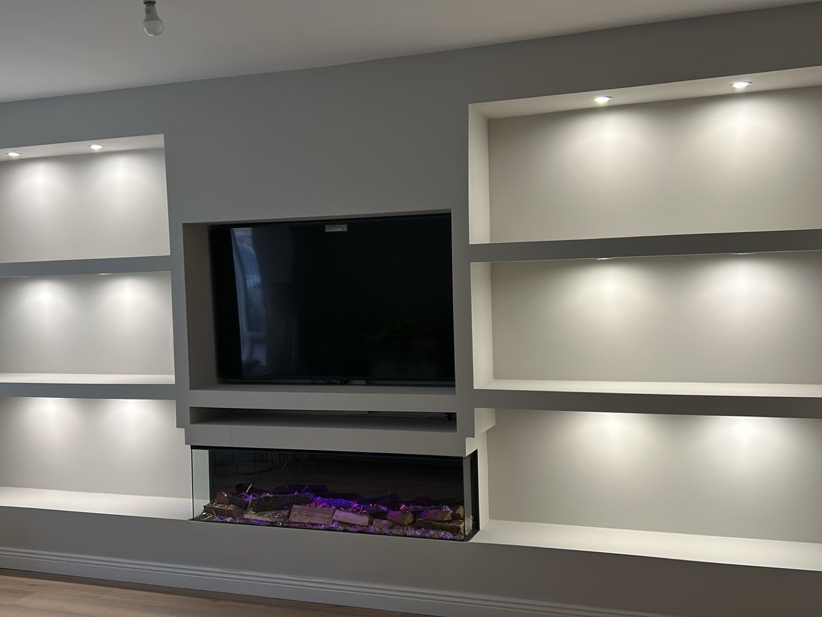 Bespoke media wall with recessed TV, floating shelves with downlights and electric fireplace built by handyman in Dublin